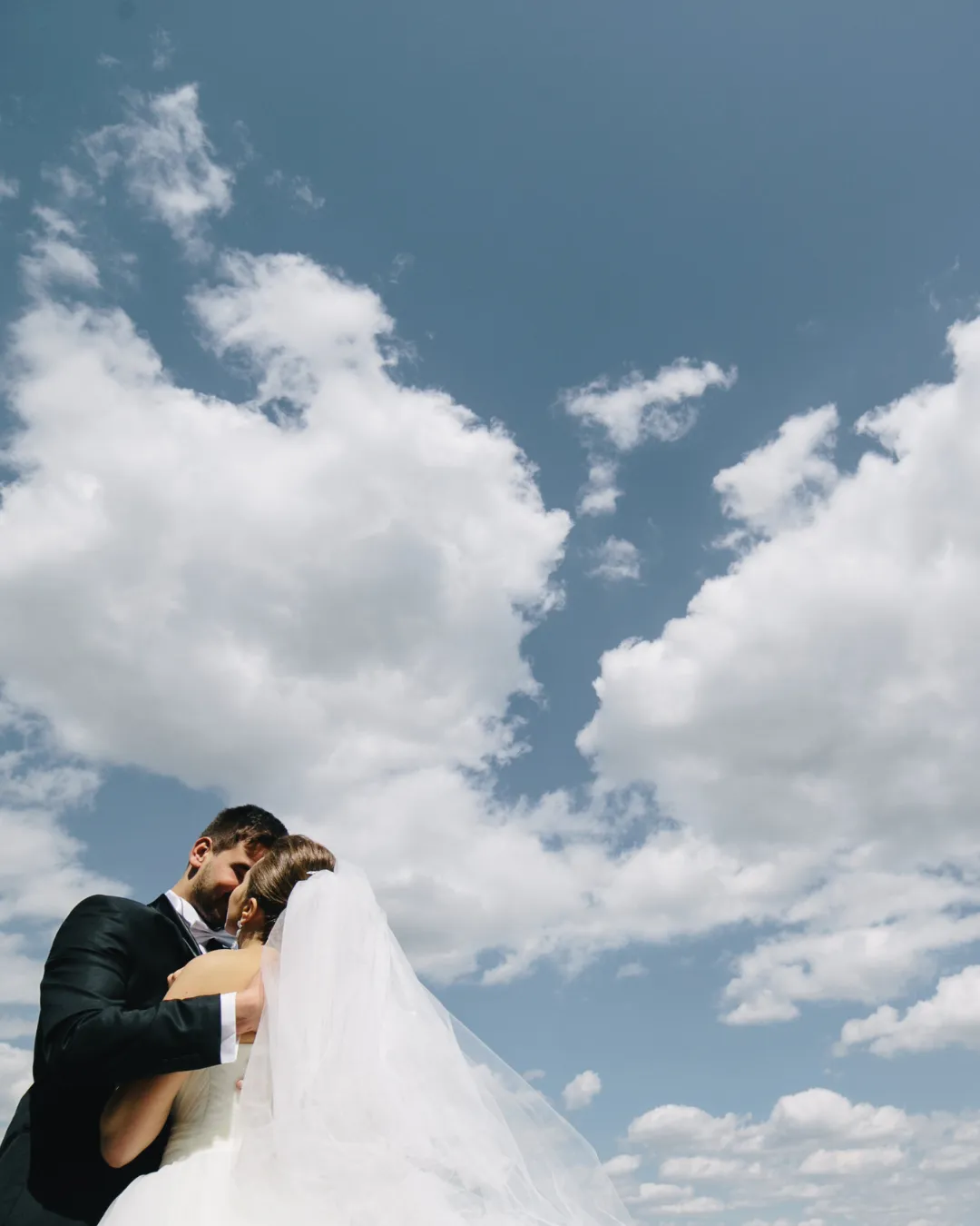 Mariée au voile et marié enlacés contre le ciel