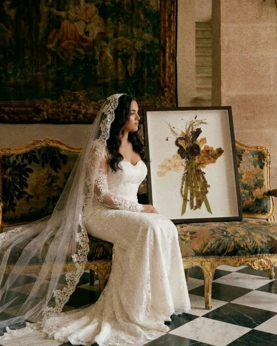 Mariée assise sur un sofa doré à côté de son bouquet préservé encadré